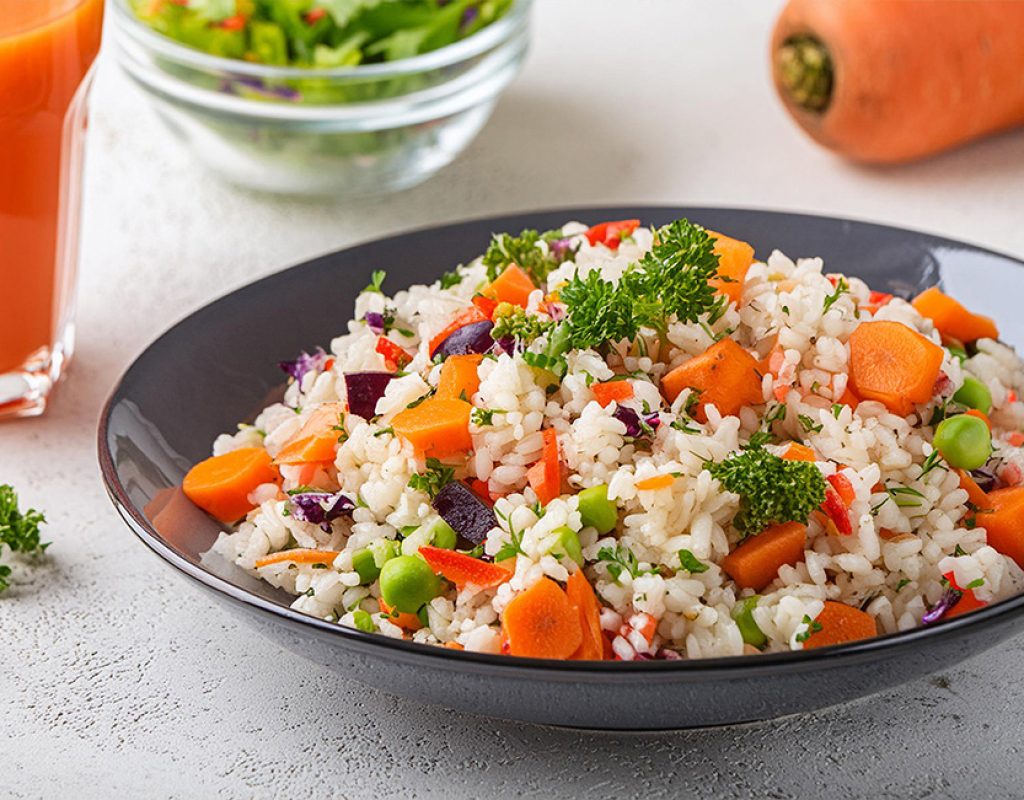 Colorful and nutritious rice salad bursting with fresh vegetables, accompained by carrot juice, offering a delectable vegan and vegetarian option for a wholesome meal choice
