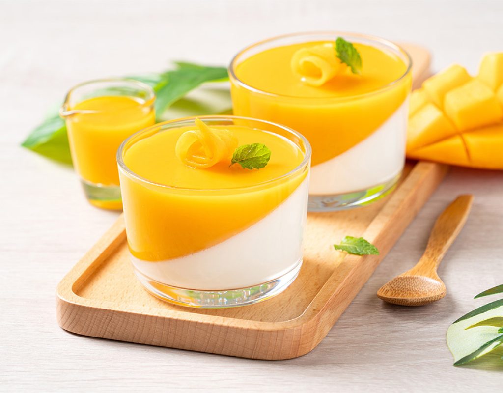 Delicious double colored mango panna cotta mousse pudding with diced mango pulp flesh topping on wooden table background.