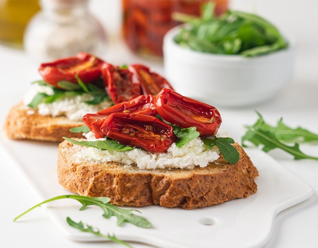 Bruschetta with sun dried tomatoes and arugula. Delicious breakfast or wine snack. White background, close-up view