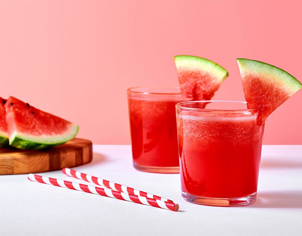 Close-up fresh watermelon juice or smoothie in glasses with watermelon pieces on pink background.