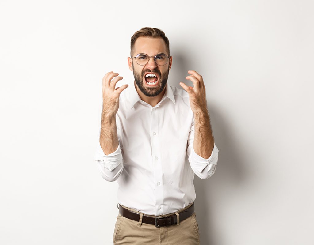 Frustrated and angry man screaming in rage, shaking hands furious, standing over white background.