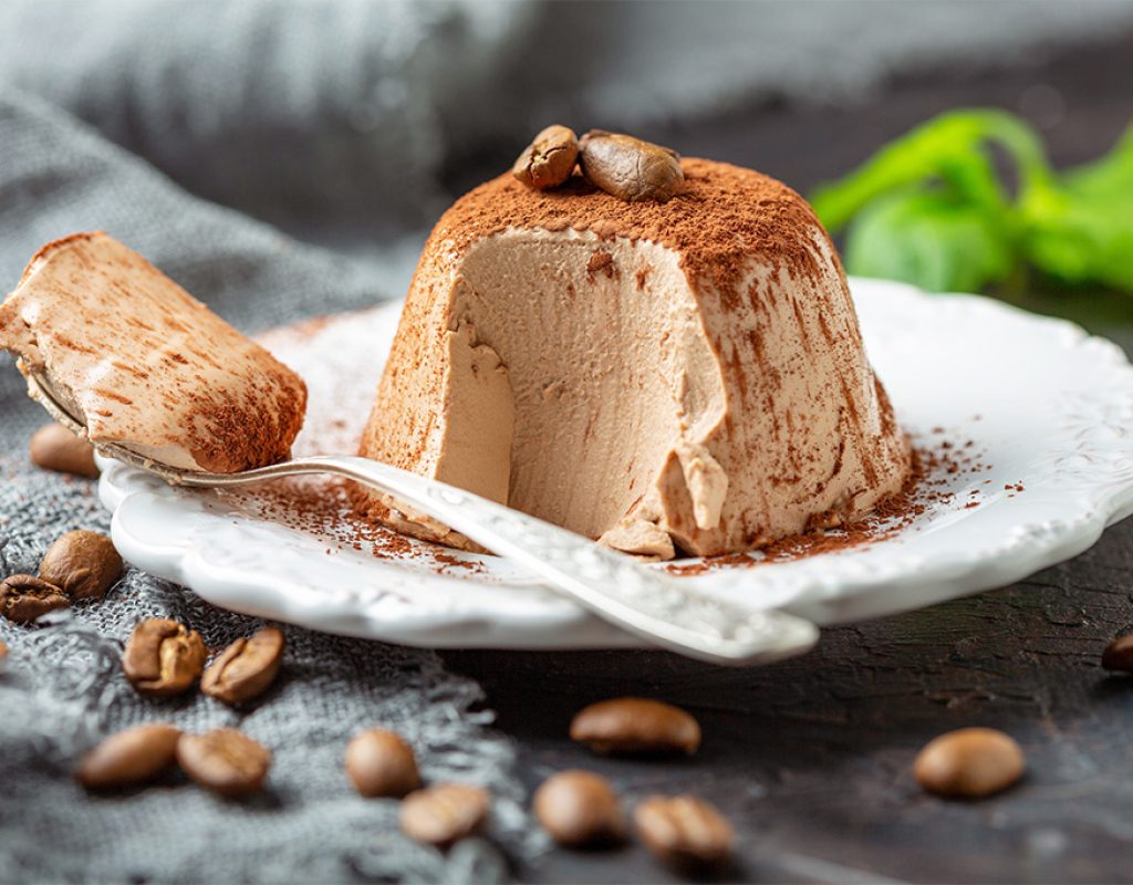 Traditional Italian dessert Panna cotta sprinkled with cocoa powder and decorated with coffee beans on a plate close-up, selective focus.