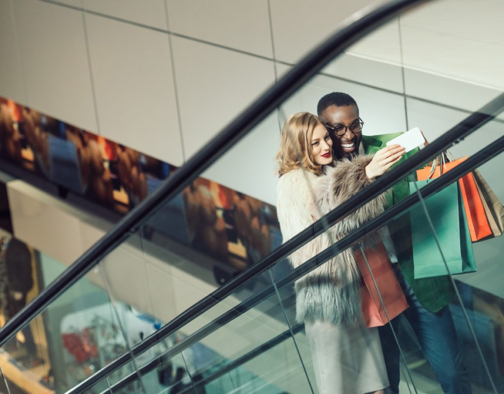 young couple taking selfie while riding escalator at shopping mall